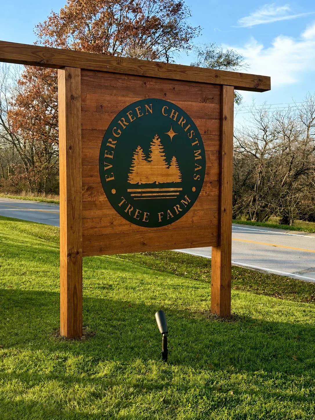 Evergreen Christmas Tree Farm roadside wooden sign with evergreen trees and a wreath.